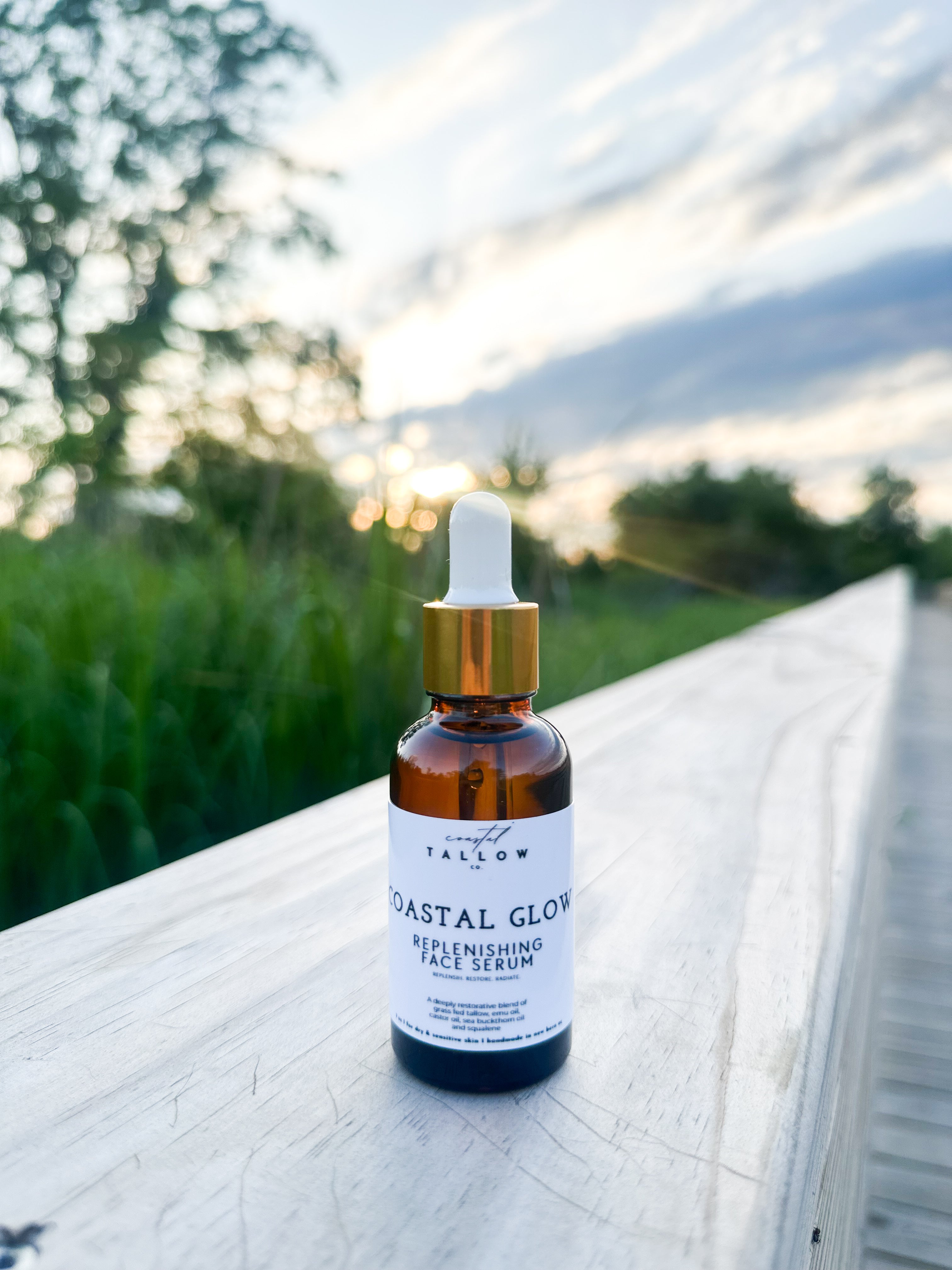 Bottle of 'Coastal Glow' replenishing face serum on a wooden surface with a natural background